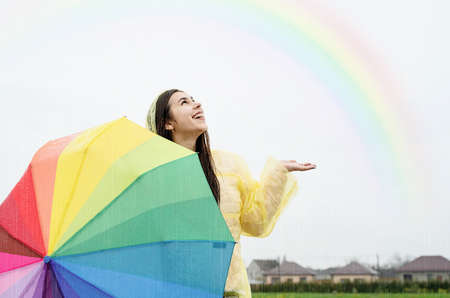 Beautiful brunette woman holding colorful umbrella out in the rainの写真素材