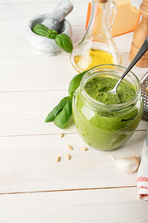 Italian cuisine. Preparing homemade italian pesto sauce. Homemade pesto sause in a glass jar with ingredients on white wooden table, copy spaceの写真素材