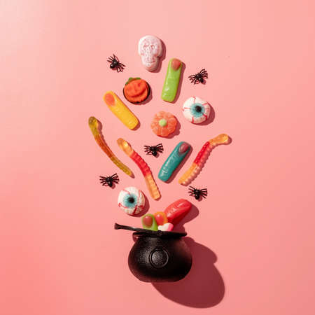 Halloween concept. Various halloween sweets in a black pot top view on pink solid background. Halloween party greeting card mock upの写真素材
