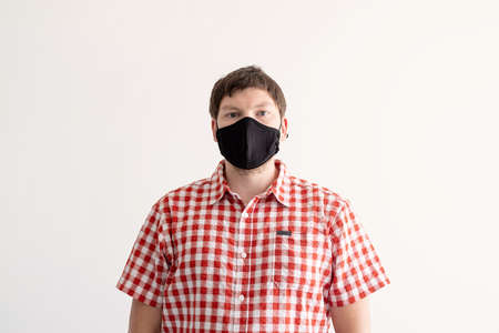 Young man in plaid shirt putting on black protection mask