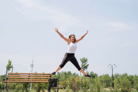 Healthy and active lifestyle. Sports and fitness. Happy woman in white t shirt working out on the sports ground in sunny summer day, stretching her legsの写真素材
