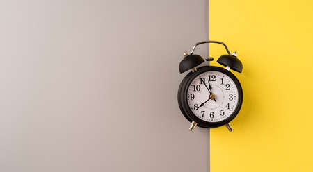 Black retro alarm clock isolated on double yellow and gray background with copy spaceの写真素材