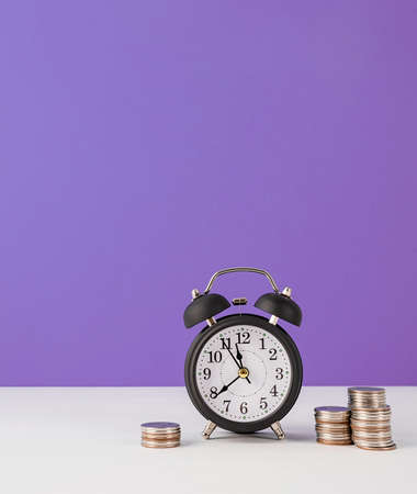 Black retro alarm clock with coins on purple background