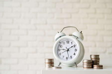 White retro alarm clock with coins on white brick wall backgroundの写真素材