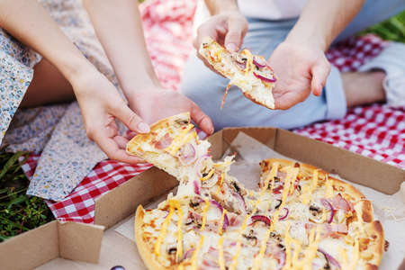 Young teenage couple in white shirts having picnic on sunflower field in sunset. Eating pizza and drinking champagneの写真素材
