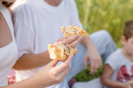 Young teenage couple in white shirts having picnic on sunflower field in sunset. Eating pizza and drinking champagneの写真素材