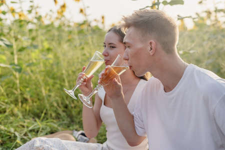 Autumn nature. Fun and liesure. Young teenage couple picnic on sunflower field in sunset drinking champagneの写真素材