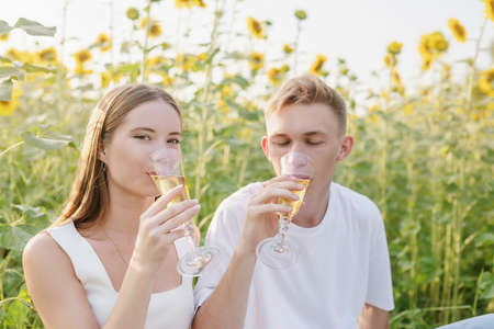 Autumn nature. Fun and liesure. Young teenage couple picnic on sunflower field in sunset drinking champagneの写真素材