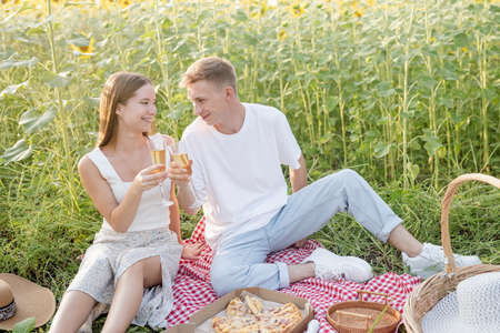 Autumn nature. Fun and liesure. Young teenage couple picnic on sunflower field in sunset drinking champagneの写真素材