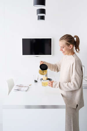 Morning routines. Young woman in comfy pajamas drinking tea at the kitchenの写真素材