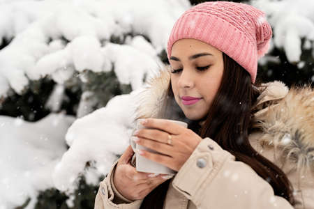 Merry Christmas and happy New Year. Beautiful woman in warm winter clothes holding mug drinking hot...