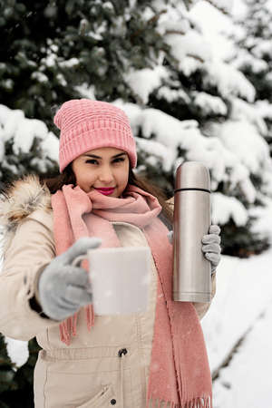 Merry Christmas and happy New Year. Happy Woman in warm winter clothes standing by the big christmas tree outdoors, arms up, snow fallingの写真素材