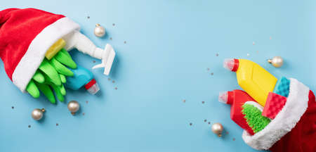 Christmas cleaning. Christmas shopping. Cleaning tools and Christmas decorations in santa hat top view flat lay on blue background with copy spaceの写真素材