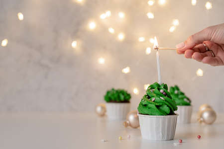 Merry christmas and happy new year. Green Christmas tree shaped cupcakes, surrounded with festive decorations and lights on the backgroundの写真素材