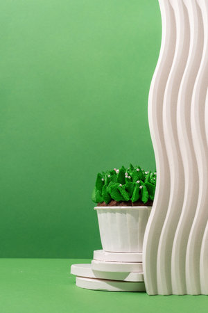 Merry christmas and happy new year. Composition of green Christmas tree shaped cupcakes on white poduims, abstract and modern minimal style, green solid background, copy spaceの写真素材
