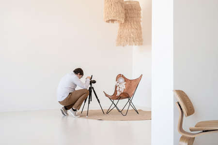 Minimal light and airy interior design. Male photographer working in minimal light and airy interior, white and beige chair, rug and pillowsの写真素材