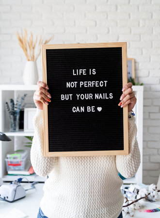 Manicure master in nail salon holding black felt letter board with text Life Is Not Perfect, But Your Nails Can Beの写真素材