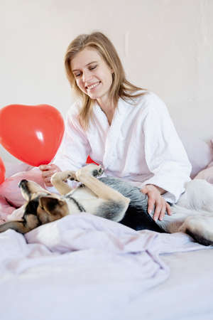 Happy valentines day. young blond woman sitting in bed with holiday gift and red confettiの写真素材