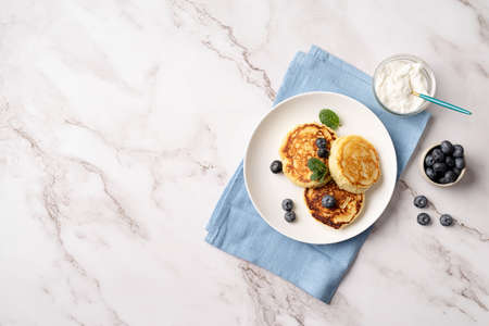Healthy calcium breakfast, lunch or snack. Cottage cheese pancakes served with sour cream and blueberries, top view flat lay on marble background, copy spaceの写真素材