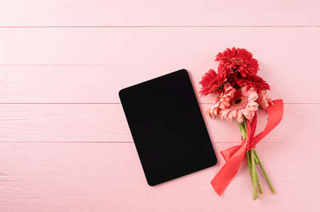 happy birthday. Red gerbera daisy flowers and digital tablet on pink wooden table, flat lay