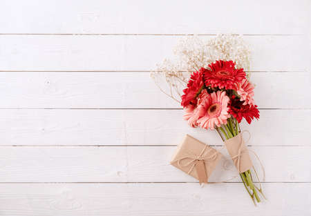 happy birthday. Red gerbera daisy flowers and craft gift box with label tag on white wooden table, flat layの写真素材