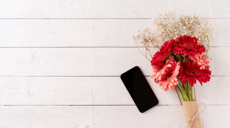 happy birthday. Red gerbera daisy flowers and mobile phone on white wooden table, flat lay