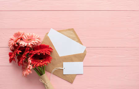 happy birthday. Red gerbera daisy flowers, envelope and blank label tag on pink wooden table