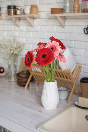 Rustic kitchen interior with white brick wall and white wooden shelves. Fresh gerbera flowers in a white vaseの写真素材