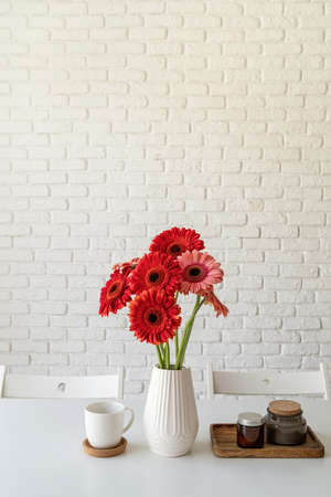 Red and pink gerbera daisies in white vase on kitchen table with candles and cup, minimal styleの写真素材