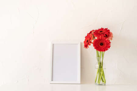 red gerbera flowers with a blank white frame on white background. mock up design