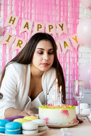 birthday party. birthday tables. Attractive brunette woman in white party clothes preparing birthday table with cakes, cakepops, macarons and other sweets, throwing pink confettiの写真素材