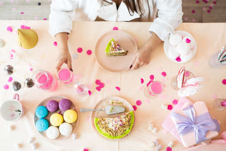 birthday party. birthday tables. Attractive brunette woman in white party clothes preparing birthday table with cakes, cakepops, macarons and other sweets, making wishの写真素材