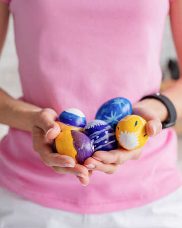 Happy Easter. portrait of young millennial woman in pink shirt coloring easter eggs in the kitchen,...