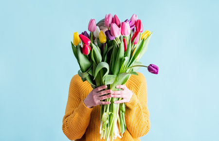 International Women's Day. pretty charming brunette young woman dressed yellow clothes holding tulip bunch isolated blue color backgroundの写真素材