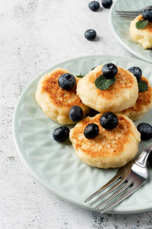 Cottage cheese fritters with blueberries on ceramic blue plate on concrete background. Healthy...