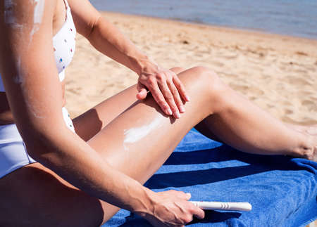 sun protection cosmetics. Young caucasian woman applying sun cream on legs sunbathing on beach