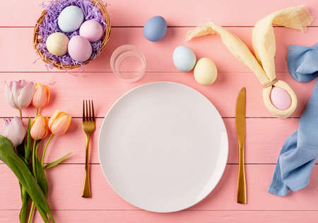 Happy Easter. Table setting for Easter feast. Easter eggs, bunny, tulips and cutlery top view flat lay on pink rustic backgroundの写真素材