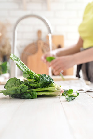 Preparing healthy foods. Healthy eating and dieting. Young smiling woman in home clothes washing spinash in the kitchen. closeup of spinachの写真素材