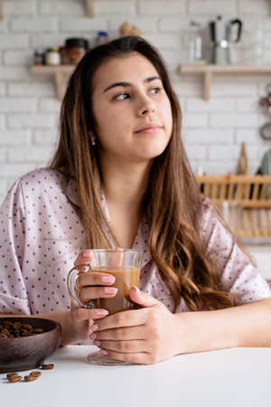 young woman in lovely pajamas drinking coffee at home kitchenの写真素材