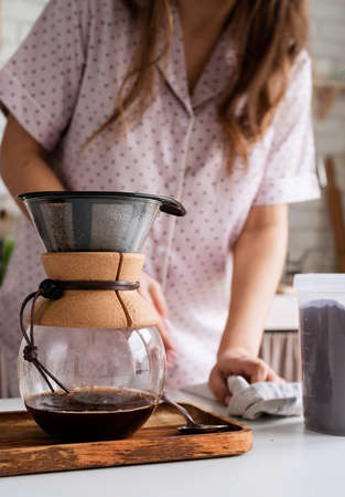 Alternative coffee brewing. young woman in lovely pajamas drinking coffee with milk at home kitchenの写真素材