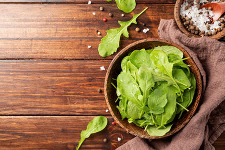 Healthy eating and dieting. Fresh arugula leaves in brown coconut bowl on wooden background top view, flat layの写真素材