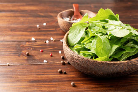 Healthy eating and dieting. Fresh arugula leaves in brown coconut bowl on wooden background with...
