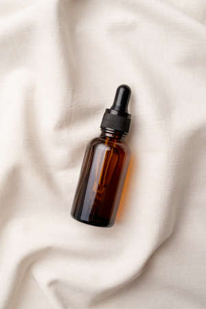 top view of amber glass essential oil dropper bottle with pipette on fabric wavy background, mockup...
