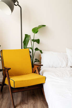 Stylish room interior with comfortable yellow chair, bed and plant near white wallの写真素材