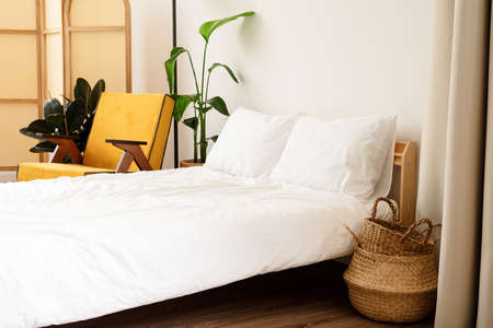 Stylish room interior with comfortable yellow chair, bed and plant near white wallの写真素材