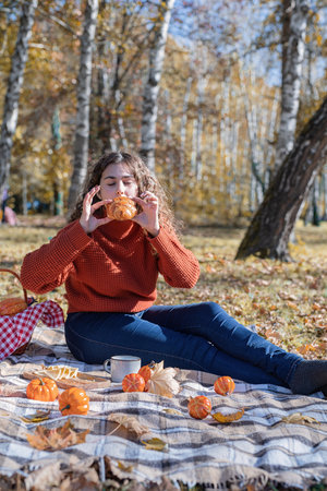 Young happy woman in red sweater having picnic in forest, eating croissantの写真素材