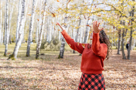 autumn nature. Young happy woman in red sweater throwing leaves in autumn forestの写真素材