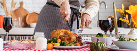 Happy Thanksgiving Day. autumn feast. Woman celebrating holiday cooking traditional dinner at kitchen with turkey, vegetables and pumpkin pie, cutting pieの写真素材