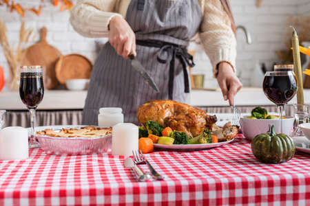 Happy Thanksgiving Day. autumn feast. Woman celebrating holiday cooking traditional dinner at kitchen with turkey, vegetables and pumpkin pie, cutting pieの写真素材