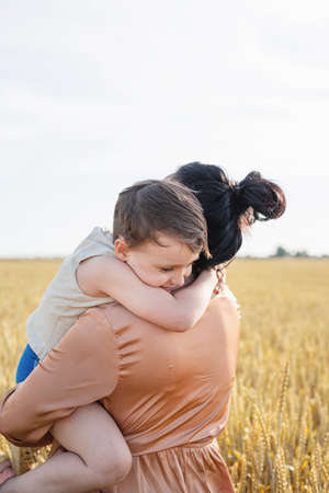 Happy family on a summer walk, mother and child walk in the wheat field and enjoy the beautiful nature, at sunset, hugging and kissingの写真素材